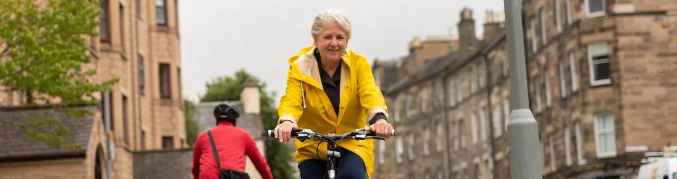 a woman in a yellow jacket cycling on a cycling lane