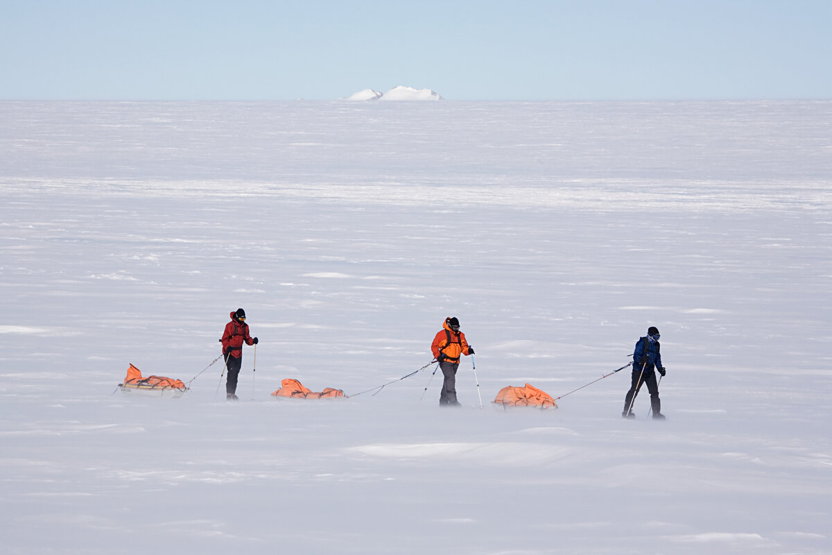 Team hauls sleds across an empty white landscape